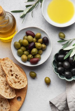 Mutfak masasında zeytin yağı şişesi, ekmek ve zeytin dalları bulunan yeşil ve siyah zeytinlerin üst görüntüsü