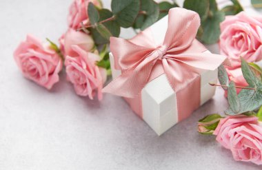 Pembe saten kurdeleli, zarif beyaz hediye kutusu ve pembe güller romantik ve şenlikli bir ortam yaratıyor.