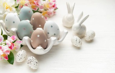 Bahar çiçekleriyle Paskalya yumurtaları ve seramik tavşanlar beyaz tahta bir masada Paskalya pazarını kutluyorlar.