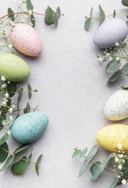 Pastel renkli paskalya yumurtaları ve okaliptüs yaprakları gri arkaplanda fotokopi alanı olan bir çerçeve oluşturuyor.