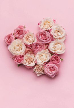Pembe ve beyaz güller pembe arka planda bir kalp şekli oluşturuyor, aşkın ve sevginin romantik bir sembolünü oluşturuyor.