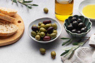 Mutfak masasında zeytin yağı şişesi, ekmek ve zeytin dalları bulunan yeşil ve siyah zeytinlerin üst görüntüsü