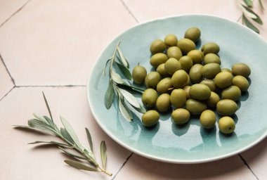 Yeşil zeytinler seramik bir tabakta sergileniyor, taze zeytin dalı ile süslenmiş, somutlaşmış Akdeniz lezzetleri ve sağlıklı beslenme