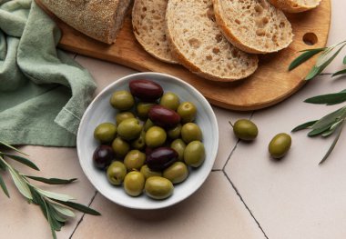 Bir kasede yeşil ve siyah zeytinli taze fırınlanmış ekmek, ahşap bir kesim tahtasında servis edilir, Akdeniz usulü atıştırmalık veya aperatif için mükemmeldir.