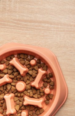 Tahta bir masaya konmuş yavaş bir yemek kasesinde kurutulmuş köpek maması. Köpekler için sağlıklı beslenme alışkanlıklarını teşvik ediyor.