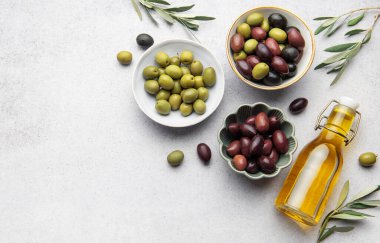 Yeşil, siyah ve kalamata zeytinleri, bir şişe zeytinyağı ve zeytin dalının yanında, Akdeniz mutfak sahnesini oluşturan kaselerde servis edilir.