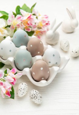 Bahar çiçekleriyle Paskalya yumurtaları ve seramik tavşanlar beyaz tahta bir masada Paskalya pazarını kutluyorlar.