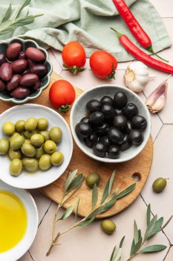Mutfak masasında çeşitli zeytinler, domatesler, sarımsak, biber ve zeytinyağı, davetkar bir mutfak sahnesi yaratıyor.