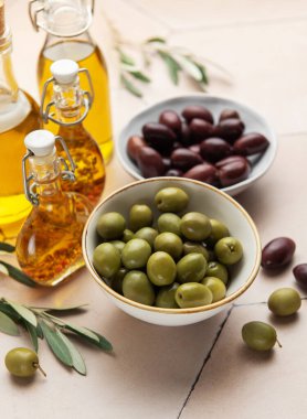 Zeytin yağı şişeleri ve zeytin dallarıyla yeşil ve siyah zeytinler bir masada oturuyorlar, sağlıklı bir aperatif ya da yemek için.