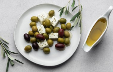 Kurabiye ve zeytinyağlı yeşil ve siyah zeytinler, geleneksel Yunan salatası için beyaz tabakta ve gri arka planda malzemeler