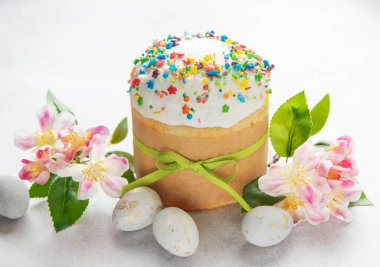 Geleneksel paskalya pastası, yeşil kurdeleyle süslenmiş rengarenk serpiştirilmiş, yanında da boyanmış yumurta ve bahar çiçekleri.