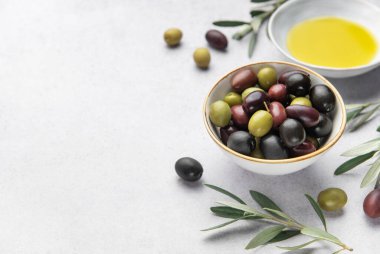 Renkli zeytinler, zeytinyağı ve zeytin dalları mermer arka planda bir Akdeniz aşçılık sahnesi oluşturur