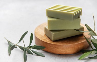 Doğal zeytin sabunları, zeytin dallarıyla ahşap ayakta dinleniyor, saflık ve tazeliği kucaklıyor.