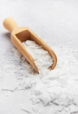 Magnezyum klorür taneleri, gri arka planda ahşap kaşıkla temizleniyor. Banyo tuzu veya diğer uygulamalarda kullanılmaya hazır.