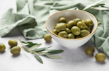 Taze yeşil zeytinler, zeytin dalı ve yeşil pamuk peçetenin yanındaki mermer masaya dizilir.