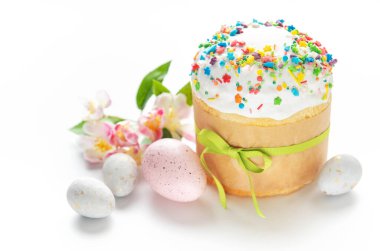 Renkli süslemeler, süslü yumurtalar ve bahar çiçekleriyle geleneksel paskalya pastası beyaz arka planda şenlikli bir süs oluşturuyor.