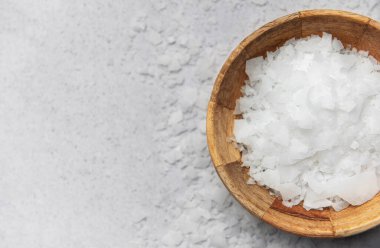 Magnezyum klorür tanecikleri, gevşeme ve kas gevşemesi için popüler bir banyo katkı maddesi, gri arka planda, ahşap bir kasede sunulur.