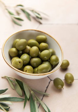 Taze yeşil zeytinler fayanslı bir yüzeyde servis edilir, zeytin dallarıyla birlikte, Akdeniz mutfağı sahnesi oluşturur.