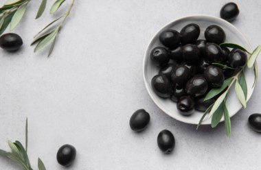 Akdeniz diyetini temsil eden gri bir zemin üzerinde zeytin dalları olan bir kasede siyah zeytin.