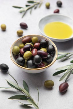Renkli zeytinler, zeytinyağı ve zeytin dalları mermer arka planda bir Akdeniz aşçılık sahnesi oluşturur