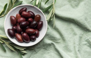 İçinde zeytin dalları olan dokulu kumaş kabında çeşitli zeytinler.