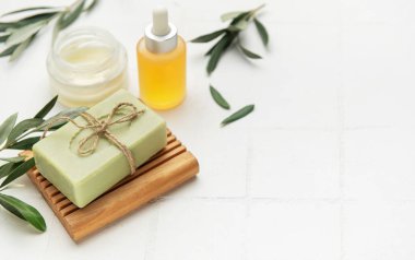 El yapımı zeytin sabunu, zeytin ağacı yapraklı krema ve beyaz arka planda doğal cilt bakımı ve spa tedavisini teşvik eden zeytin ağacı yaprakları.