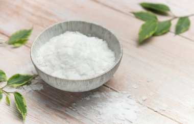 Magnesium bath flakes in a bowl on a wooden table with green leaves, promoting relaxation and wellness
