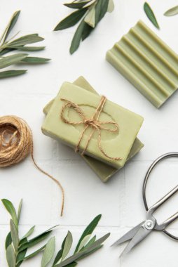 Beyaz karo arka planda dizilmiş sicim, makas ve zeytin dallarıyla bağlanmış el yapımı zeytin sabunları atmosfer gibi kırsal, spa
