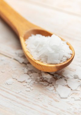 Magnesium chloride flakes resting on wooden spoon on white wooden table