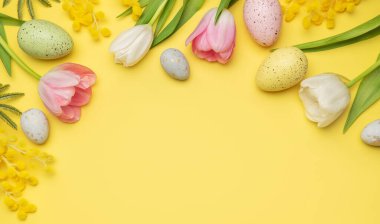 Paskalya yumurtaları ve bahar çiçekleri kopya alanı olan sarı arkaplanda bir çerçeve oluşturuyor.