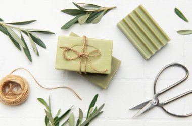 Beyaz karo arka planda dizilmiş sicim, makas ve zeytin dallarıyla bağlanmış el yapımı zeytin sabunları atmosfer gibi kırsal, spa