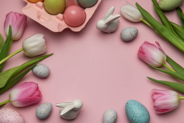 Paskalya yumurtaları, seramik tavşanlar ve laleler pembe arka planda fotokopi alanı olan bir çerçeve oluşturuyorlar.