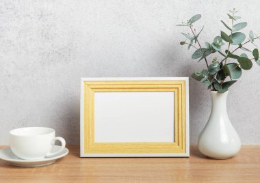 Boş çerçeveli modern ev dekoru, kahve fincanı ve okaliptüs dalları ahşap bir masa üzerinde vazoda.