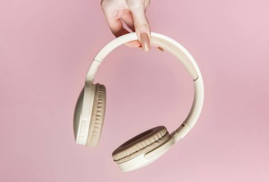 Pembe arka planda cilalanmış tırnakları olan bir elin kablosuz kulaklığı.