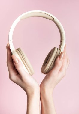 Pembe arka planda modern kablosuz kulaklıkları tutan kadın eller, müzik dinleme konsepti