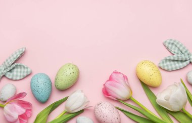 Paskalya yumurtaları ve laleler pembe arka planda fotokopi alanı olan bir çerçeve oluşturuyor.
