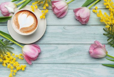 Turkuaz ahşap arka planda latte sanat ve bahar çiçekleriyle kapuçino. Aşkı, anneler gününü ve baharı kutlamak için.