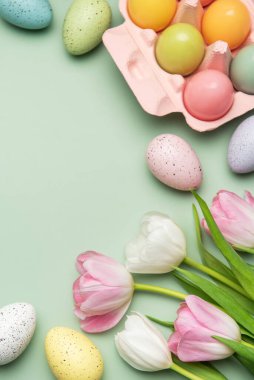 Renkli paskalya yumurtaları ve pembe ve beyaz laleler pastel yeşil arka planda fotokopi alanı ile bahar hissi yaratıyor.