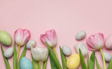 Pembe arka planda sıralanmış renkli Paskalya yumurtaları ve laleler neşeli bir bahar sınırı oluşturur.
