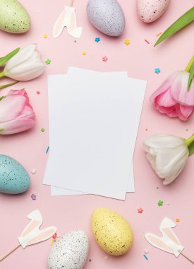 Renkli yumurtalar, laleler ve pembe arka plandaki tavşan kulaklarıyla çevrili Paskalya tebrik kartı modeli bahar kutlamaları için mükemmeldir.
