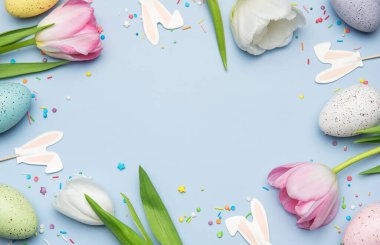 Paskalya yumurtaları, laleler ve tavşan kulakları açık mavi arkaplanda fotokopi alanı ile bir çerçeve oluşturuyor.