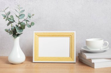 Şık İskandinav iç tasarımı. Fotoğraf çerçevesi, okaliptüs yaprakları, ahşap masa üzerinde kitaplar ve kahve fincanı.