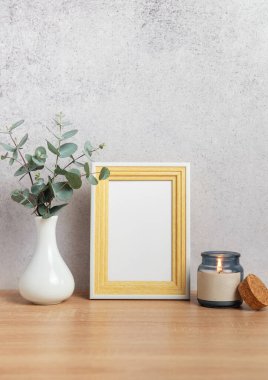 Ahşap çerçeve, yanan mum ve okaliptüs dalları ile ahşap masada gri duvara yaslanmış vazoda.