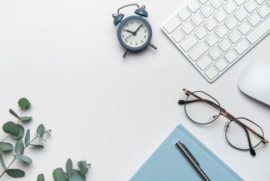 Merkez ofis masası beyaz masadaki bilgisayar klavyesi, fare, defter, kalem, gözlük ve alarmla çalışmaya hazırlanıyor.