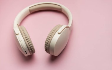 Müzik, teknoloji ve kişisel ses zevkini temsil eden canlı pembe bir fon üzerinde dinlenen şık kulaklıklar.