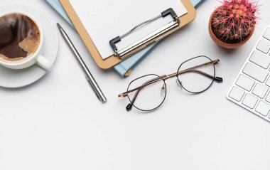 Kahveli, panolu, gözlüklü, kalemli, klavyeli ve kaktüslü beyaz ofis masası verimli bir gün için davet edilen işyeri.