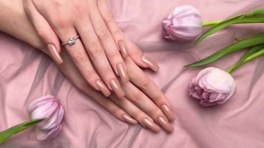 Mükemmel kahverengi manikürlü kadın elleri pembe arka planda lalelerle