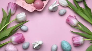 Pembe laleli Paskalya süslemeleri, renkli yumurtalar ve pembe arka planda neşeli bir çerçeve oluşturan tavşan heykelcikleri.