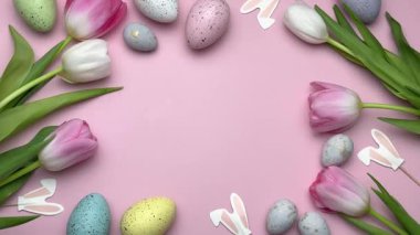 Pembe laleli Paskalya süslemeleri, renkli yumurtalar ve pembe arka planda neşeli bir çerçeve oluşturan tavşan heykelcikleri.