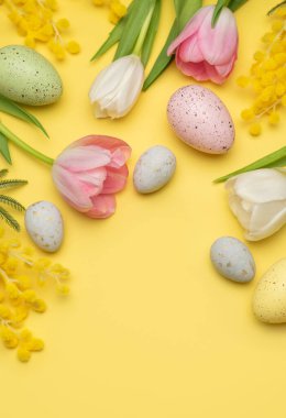 Paskalya yumurtaları ve bahar çiçekleri kopya alanı olan sarı arkaplanda bir çerçeve oluşturuyor.